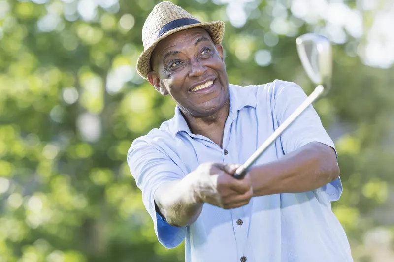 An older man swings a club on the golf course.
