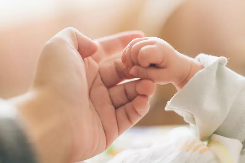 A baby holding one of her mother's fingers