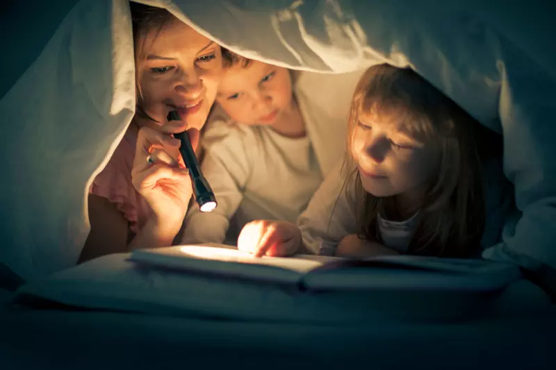 A mother, daughter, and son reading bedtime stories underneath the sheets