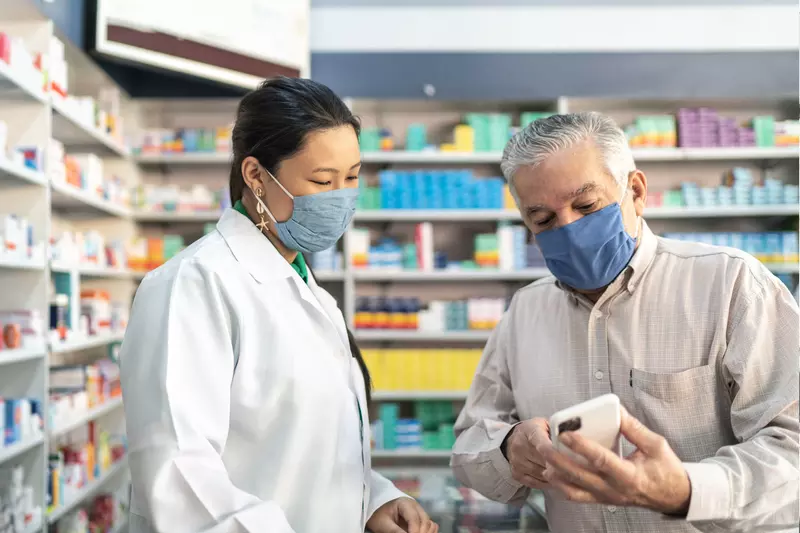 Older man talking with a pharmacist while both wear masks.