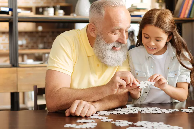 A grandfather puts together a puzzle with his granddaughter. 