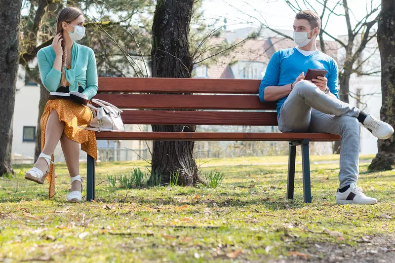 Two people keeping their distance on a park bench.