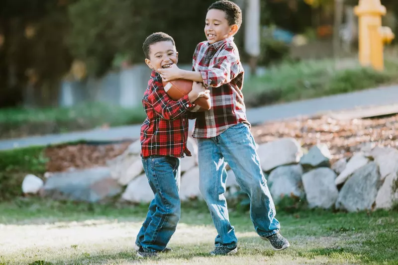 Two young boys playing football outside.