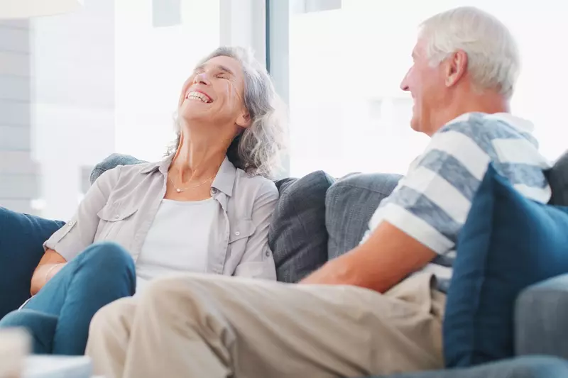 A woman laughing while sitting on the couch with her spouse.