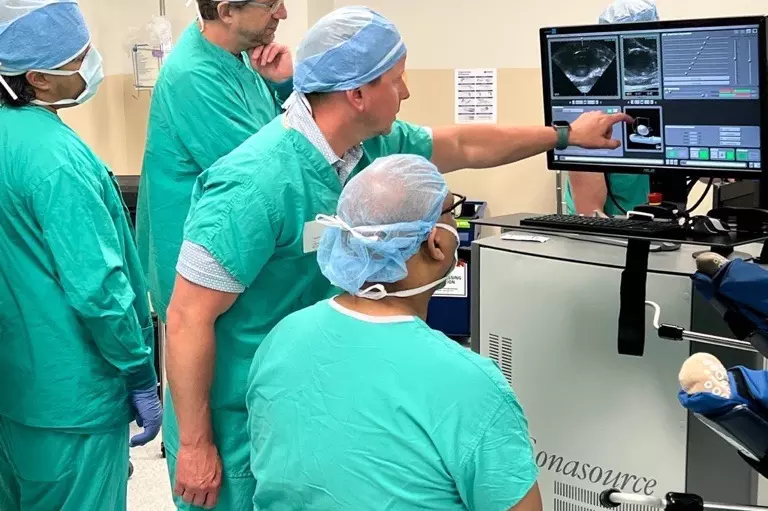 People in scrubs in operating room, pointing to screen.