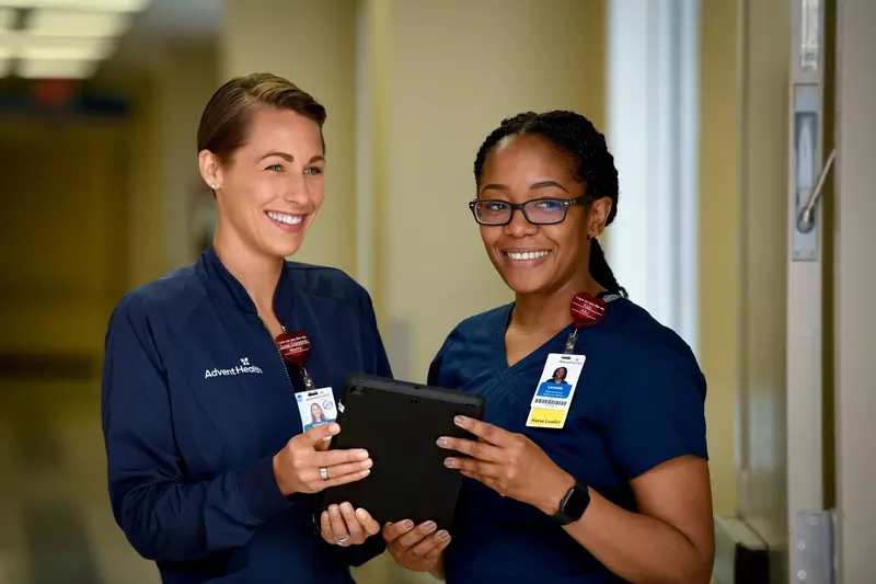 Two nurses from AdventHealth holding a tablet
