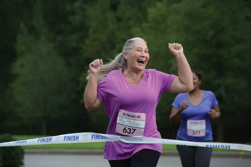 An older woman is ecstatic as she crosses the finish line of a charity foot race