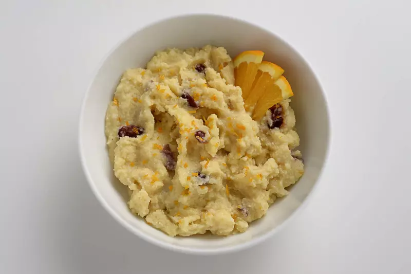 a bowl of polenta with dried cranberries and orange slices