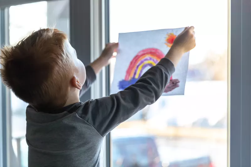 A child holding up a rainbow drawing. 