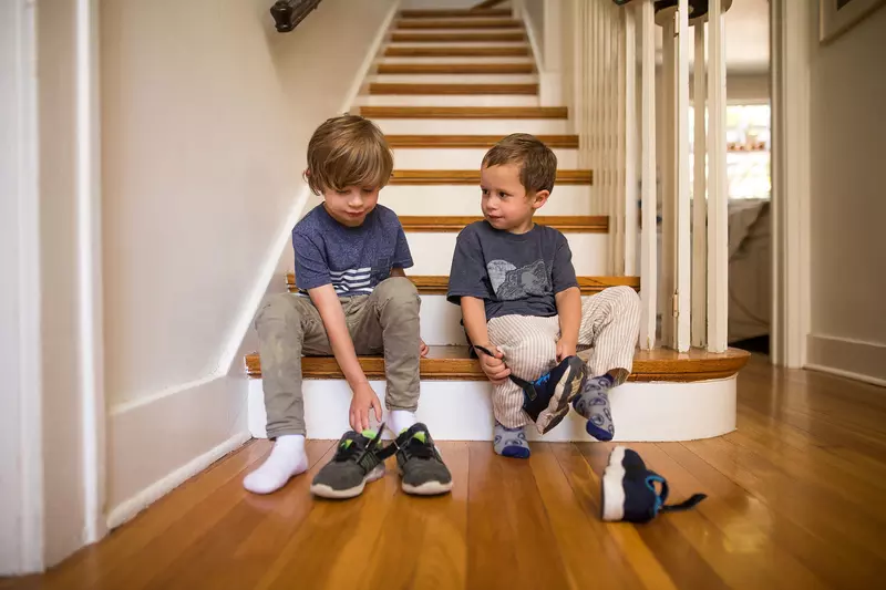 Two brothers getting ready to go out while putting their shoes on.