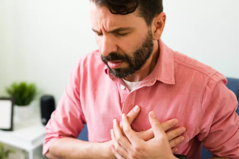 A main sitting and placing hands over chest in pain.