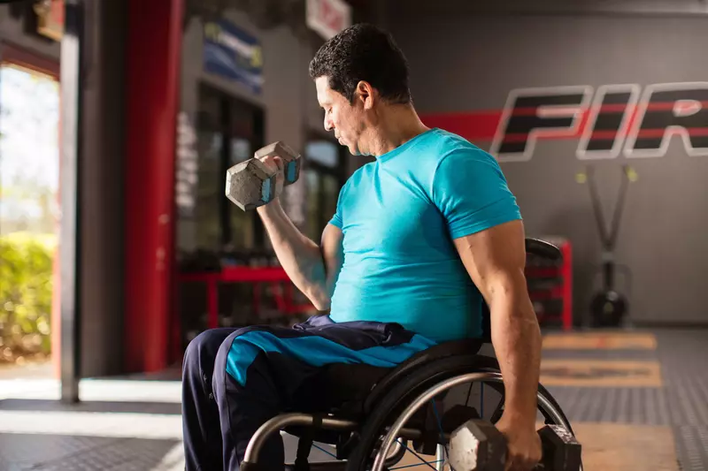 Man in a wheelchair lifting a dumbbell weight with his right hand. 