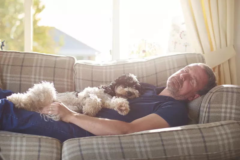Man napping on a couch with a dog.