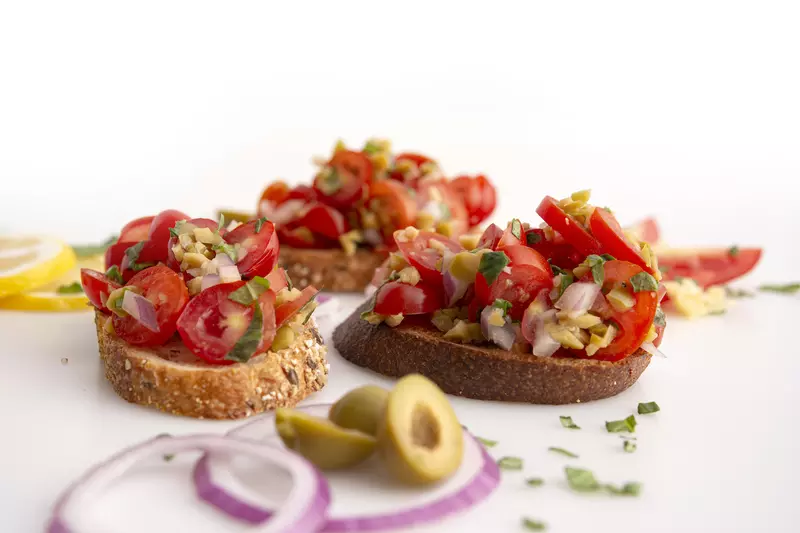 three pieces of bruschetta-topped toast with olive garnish