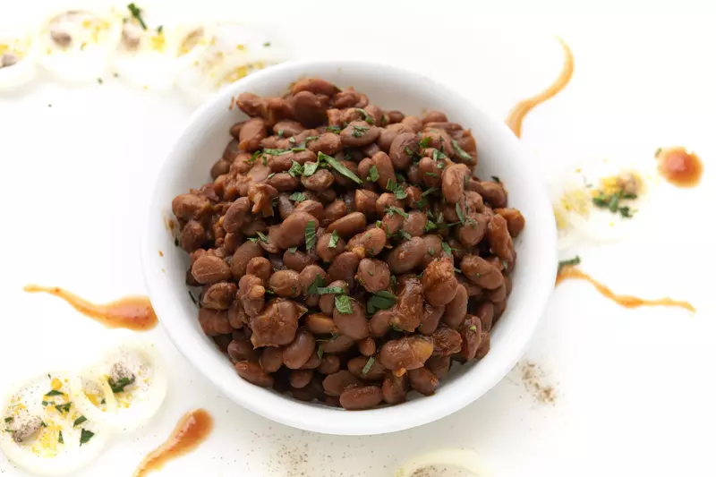 White bowl of baked beans on white, garnished counter