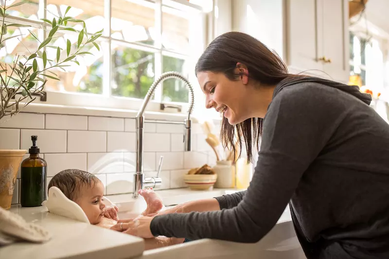 A mom bathing her new born in the kitchen sink. 