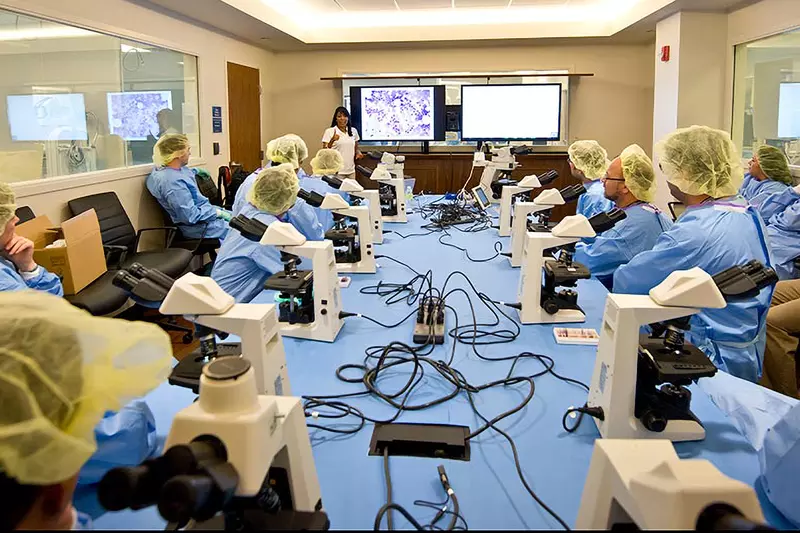Professionals attending a lecture with microscopes in a Nicholson Center Lab Boardroom.