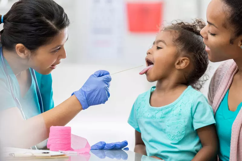 A female nurse examines the tonsils of a young girl at a doctor appointment.