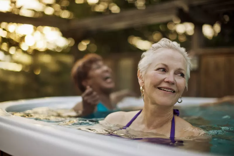 Two women laugh while soaking in an outdoor spa