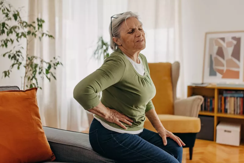 An older woman, sitting at home, holding her side in pain.