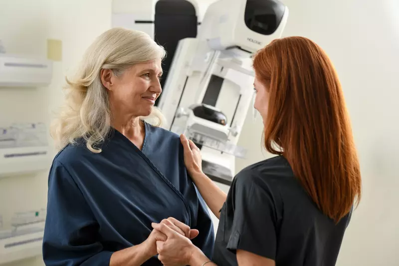 Woman with a technician before a mammogram standing in front of a mammography machine.