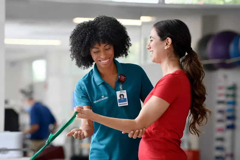 Physical Therapist guiding a woman patient through an exercise to strengthen arm.