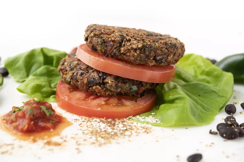 Two stacked bean burgers patties, sliced tomatoes, and lettuce leaves