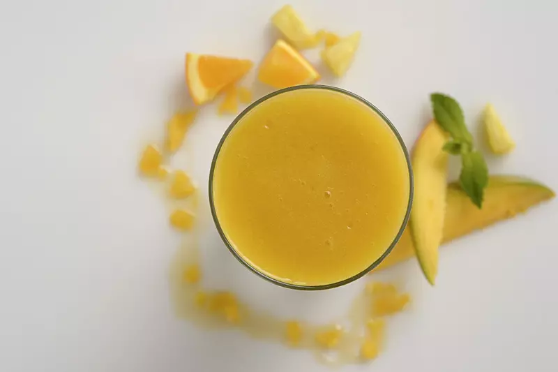 an overhead shot of a clear glass filled with pineapple-mango smoothie