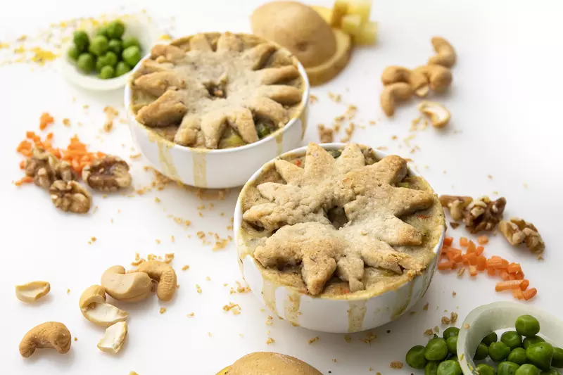 Two ramekins of pot pie on white surface with pea and cashew garnishes 
