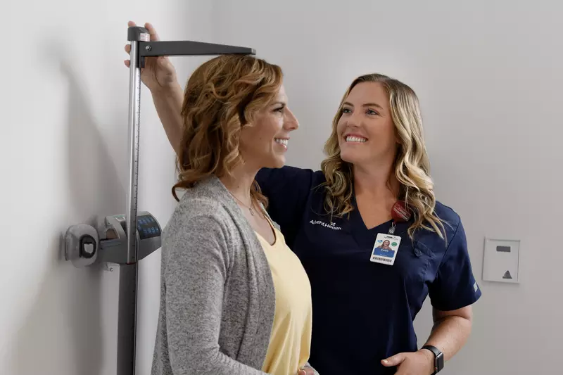 A Primary Care+ Nurse Measures the Height of a Smiling Patient