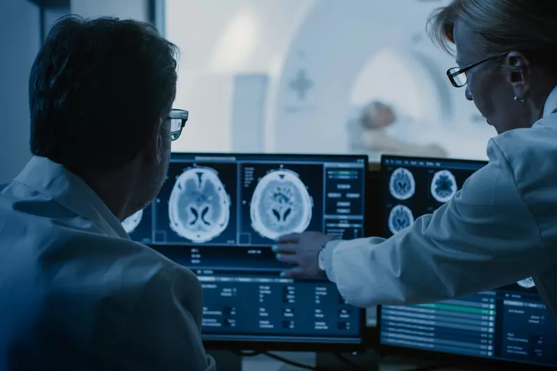 Radiologists looking at a brain scan while a patient is getting a CT scan.