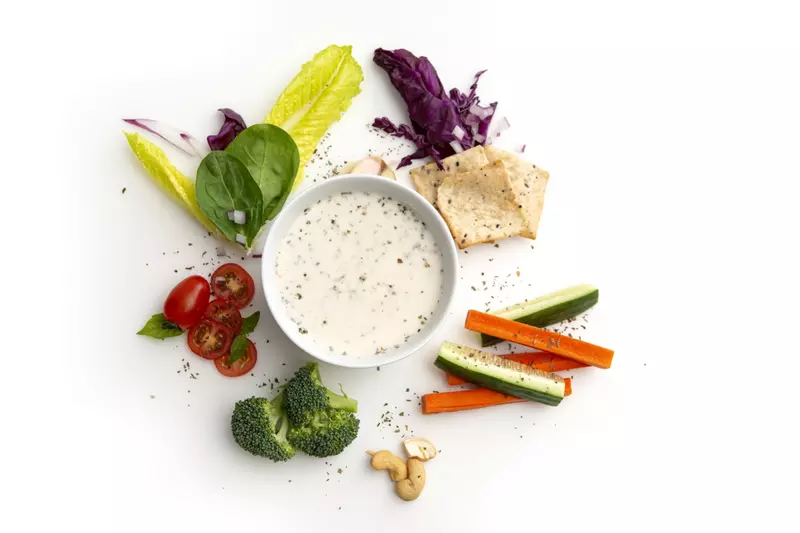 Cup of creamy ranch-style dressing surrounded by vegetables