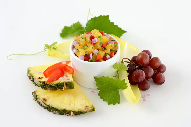 Dish of pineapple and jalapeno salsa surrounded by grapes and greens