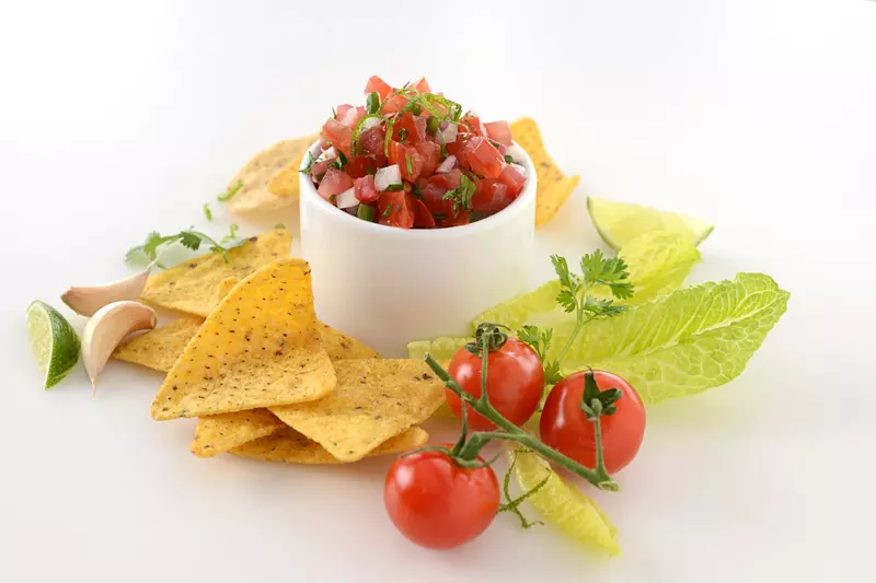 Dish of rustic tomato salsa surrounded by chips, garlic and tomatoes