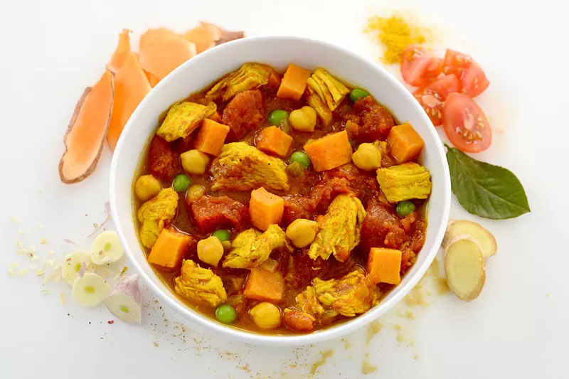 Dish of sweet potato and chicken curry surrounded by chopped potatoes and veggies