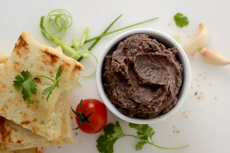 mashed black beans in a bowl, surrounded by tomatoes, bread, garlic and herbs