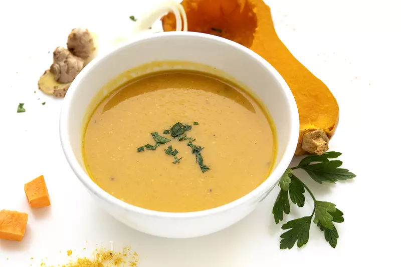 Bowl of squash soup with half butternut squash and green sprig garnish on side