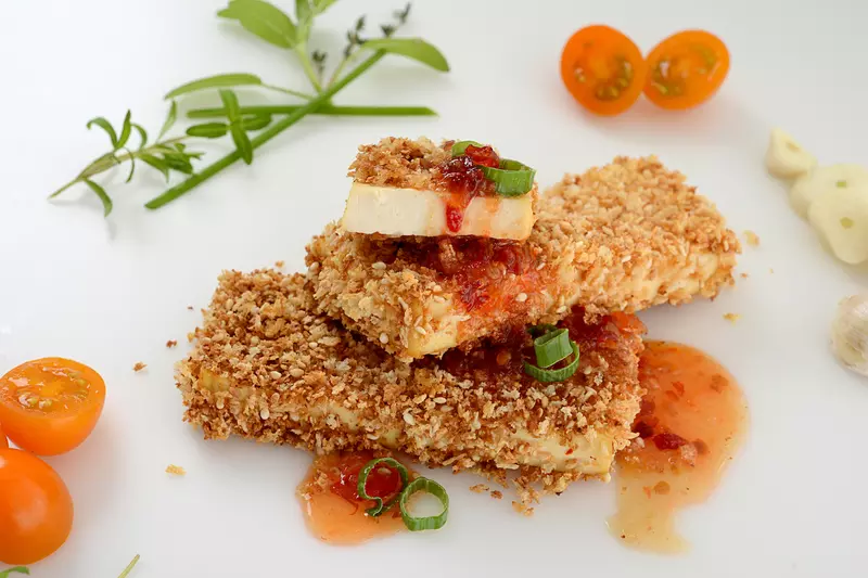 Two and a half crusted tofu steaks with herb and tomato garnishes