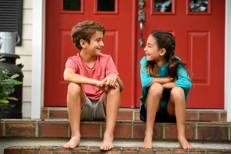 A boy and girl make jokes while sitting on their porch