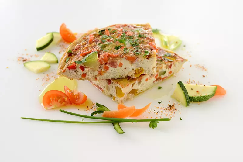 two slices of a veggie-packed omelet, surrounded by additional slices of zucchini and tomato 