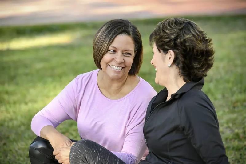Two smiling women sitting outdoors talking