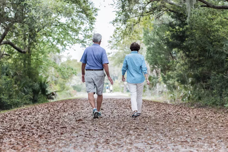 An elderly Caucasian couple takes an afternoon walk on a trail.