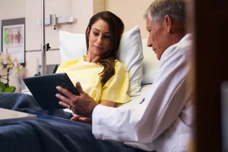 A male doctor goes over a female patient's results on a tablet in her hospital room.
