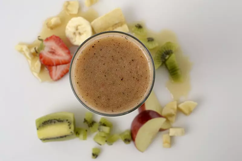 blended fruit in a glass, surrounded by slices of strawberry, banana, kiwi and red delicious apple
