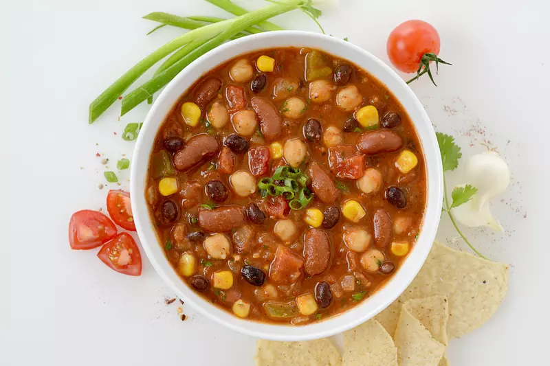 Bowl of three bean chili with corn and tomato and chive garnishes