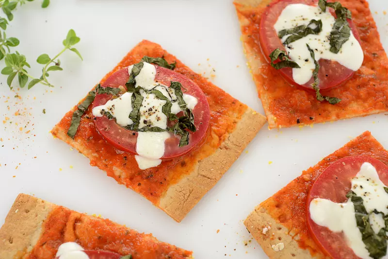 Four square pieces of margherita pizza with green garnish.