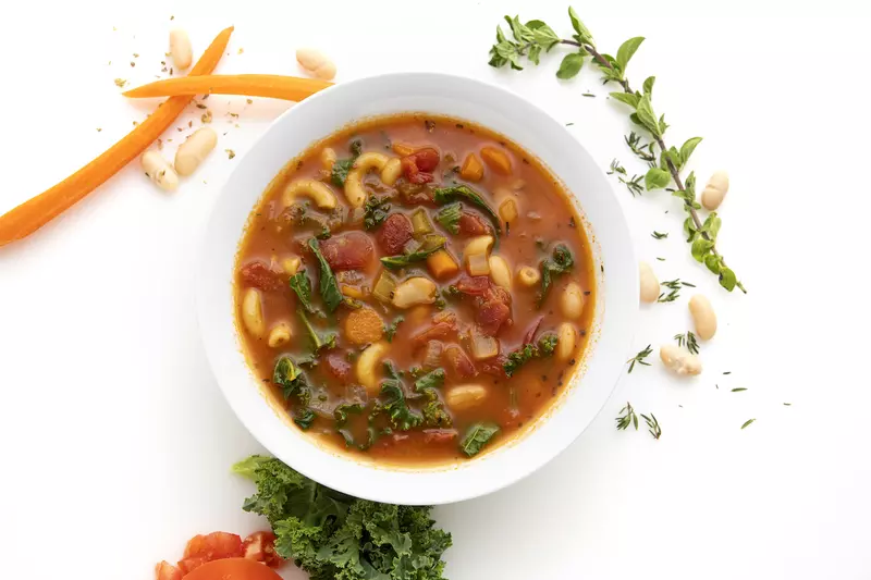 Bowl of white bean and kale soup with carrot and herb garnishes