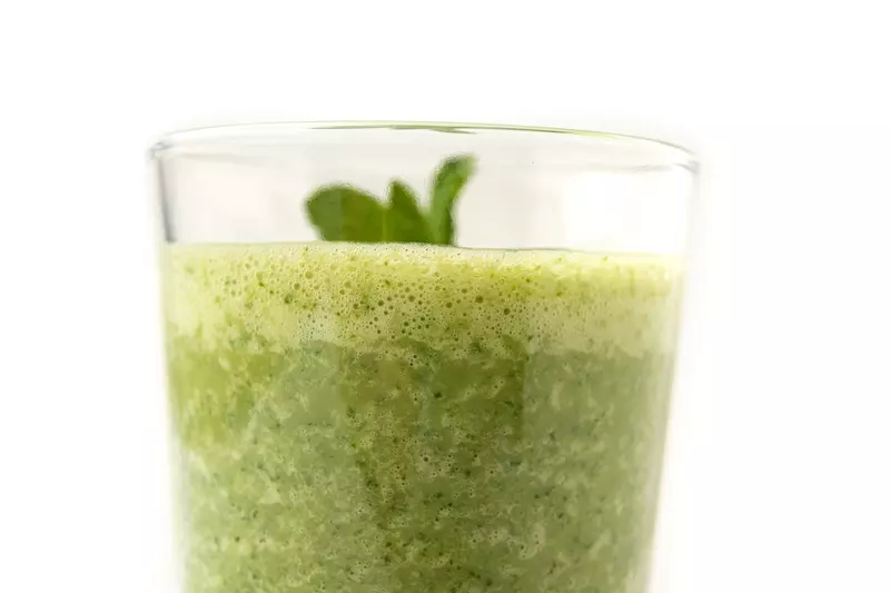 Clear glass of green smoothie with sprig on top