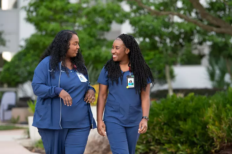 Two nurses walking outdoors and talking together.