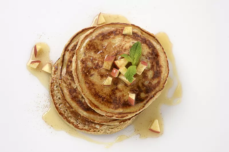 a stack of three homemade pancakes, topped with cubed apples